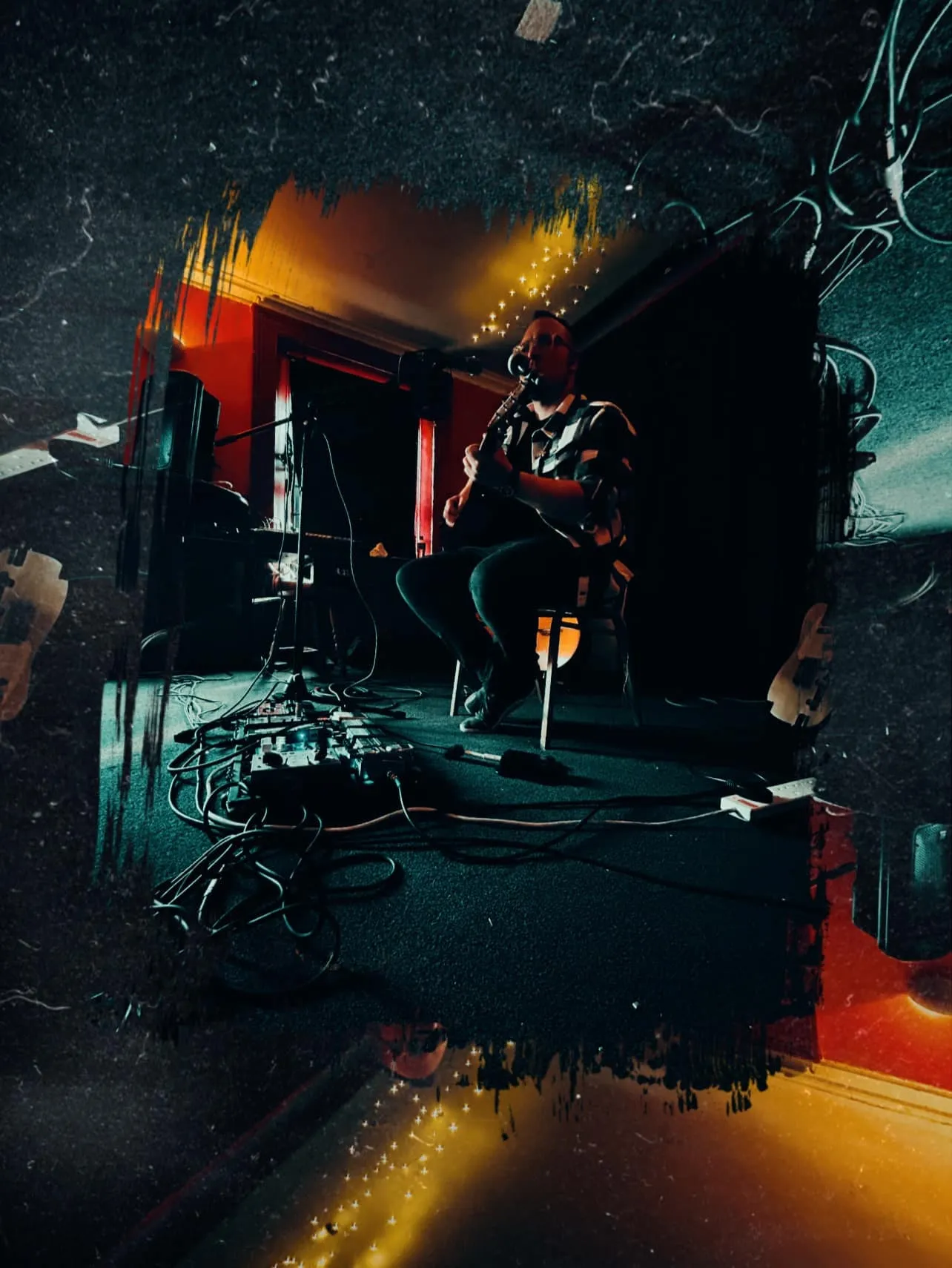 Isaac Birchall playing acoustic guitar on a small stage at Anseo, Dublin, in 2024, lit in red and amber.