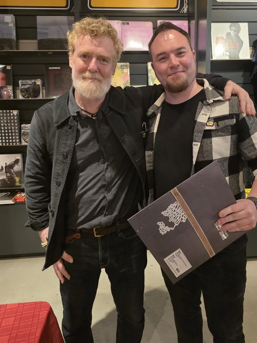 Isaac Birchall standing with Glen Hansard, who has an arm around his shoulder and a guitar at his side.