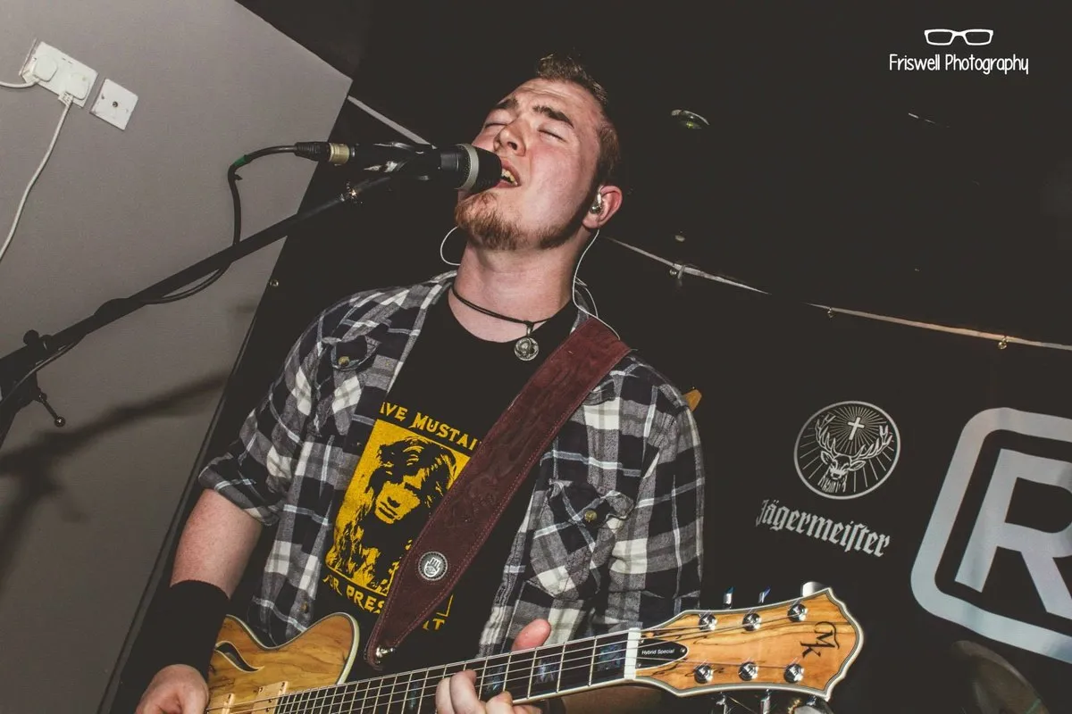 Isaac Birchall singing into a microphone with an electric guitar, Rewind and Jagermeister signage behind him.